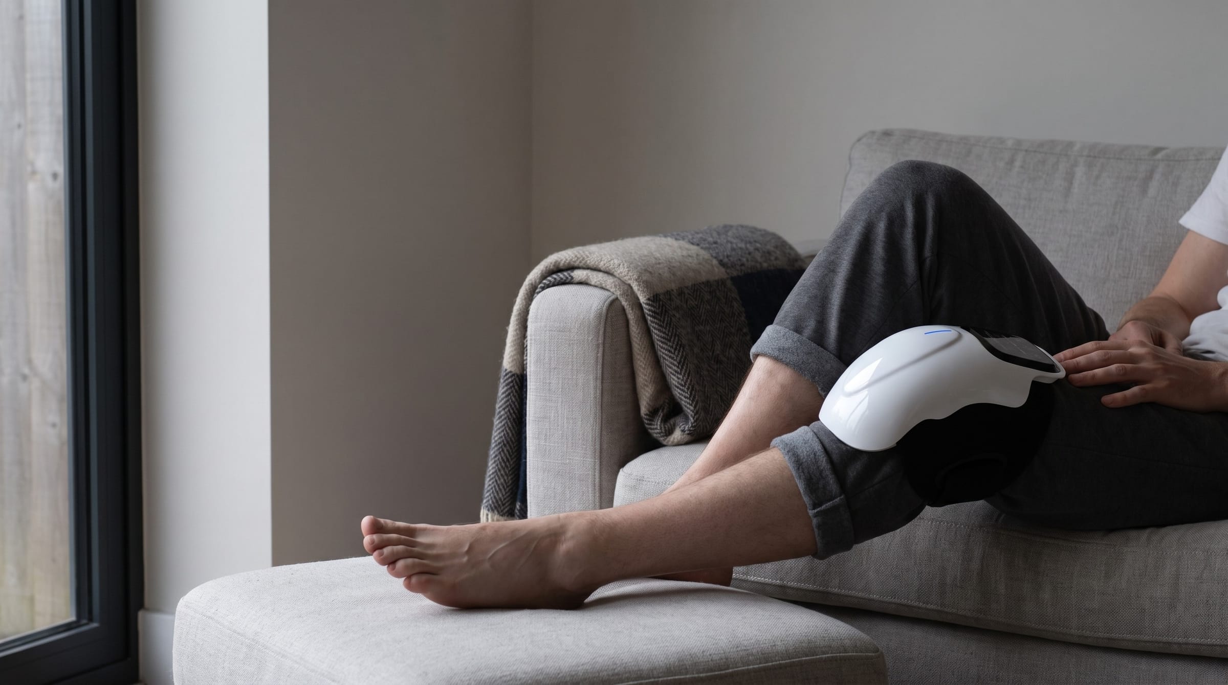 Someone on a grey couch with the heated knee massager strapped over one knee